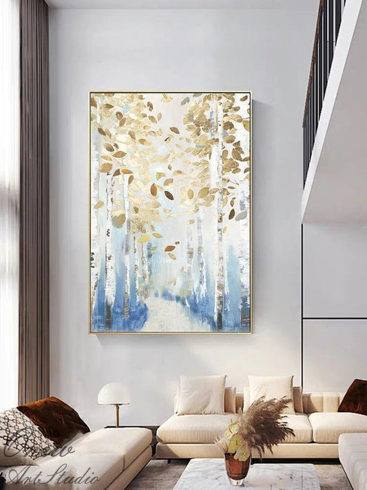 May include: Large framed abstract painting featuring a forest scene with gold and brown leaves. The artwork has a gold frame and a color palette of white, blue, and gold. The painting is displayed in a modern living room setting.