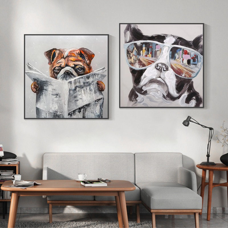 May include: Two framed paintings of dogs. The painting on the left shows a brown and white bulldog reading a newspaper. The painting on the right shows a black and white bulldog wearing sunglasses with a city reflected in the lenses.