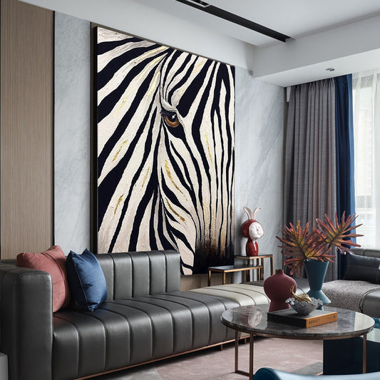 May include: Large framed artwork featuring a close-up of a zebra's face. The painting has bold black and white stripes with gold accents. The zebra's eye is visible, adding detail to the artwork. The artwork is displayed in a modern living room setting.