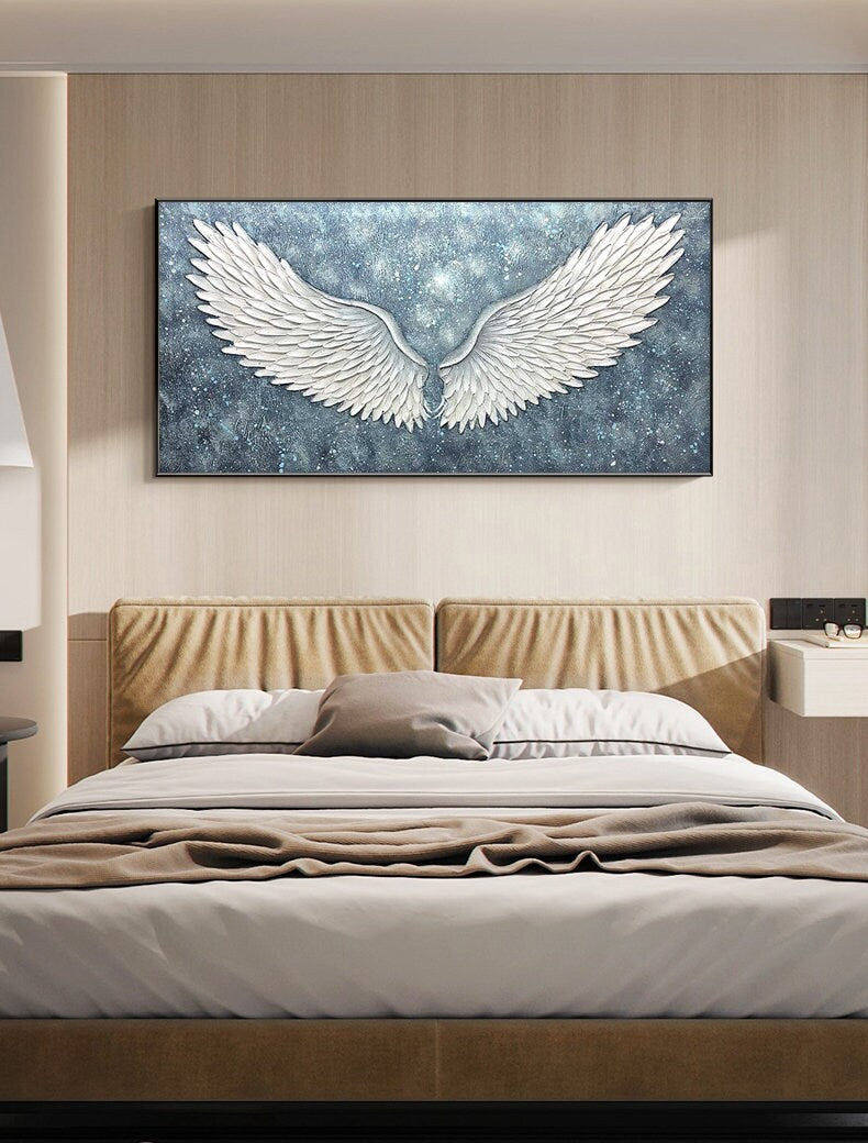 May include: A white canvas painting of a pair of angel wings against a blue and white starry background. The wings are large and detailed, with a 3D effect.