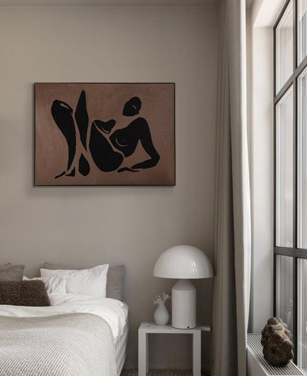 May include: A black and white abstract line drawing of a person in a reclining pose on a brown background. The drawing is framed and hanging on a wall in a bedroom.