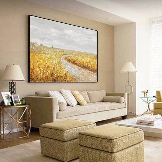 May include: A painting of a winding dirt road through a field of golden wheat. The sky is a light gray with white clouds. The painting is framed in a black frame and is hanging on a wall in a living room.