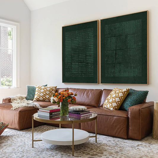 May include: Two large rectangular wall art pieces featuring a dark forest green textured surface with vertical and horizontal line patterns, each framed in a light wood border, displayed side by side on a white wall above a brown leather sofa.