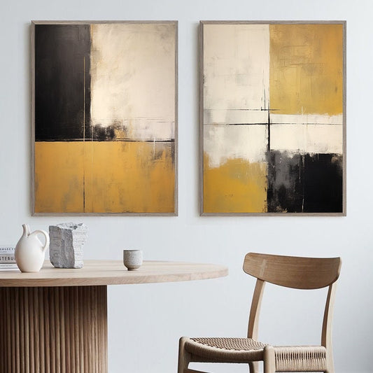 May include: Two abstract paintings with a geometric design in shades of black, white, and gold. The paintings are framed in a light wood frame and are hanging on a white wall.