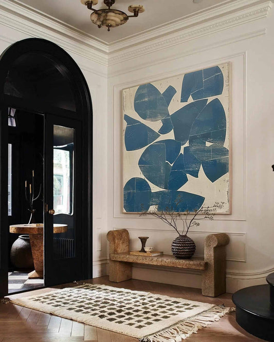 May include: An interior hallway featuring a large abstract painting with blue shapes on a cream background. A stone bench with a decorative vase and a patterned rug are in front of the painting. A black arched doorway leads to another room.