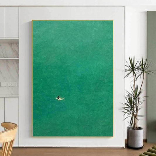 May include: A minimalist abstract painting of a person on a surfboard in a turquoise ocean. The painting is framed in a thin gold frame.
