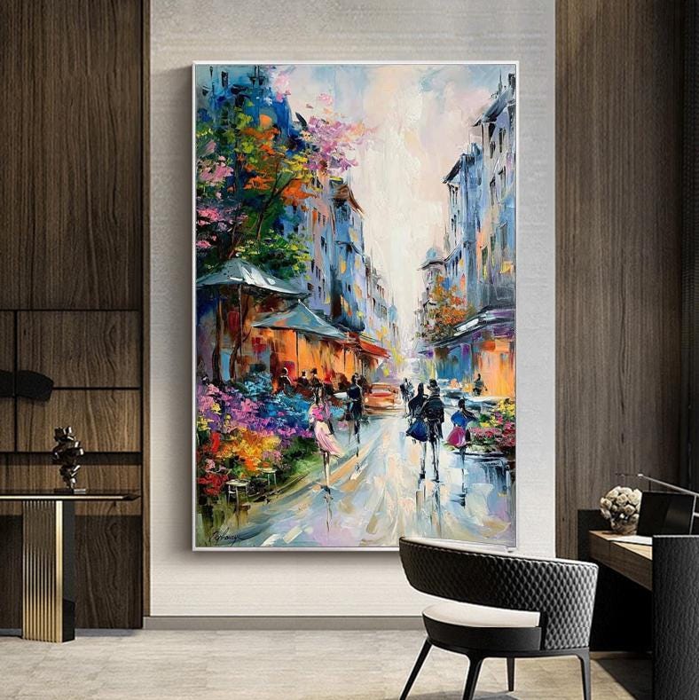 May include: An oil painting depicts a European street scene with buildings in shades of blue and orange. The artwork features a wet street reflecting the colors of the buildings and the people walking along the sidewalk. Colorful flowers and trees line the street.