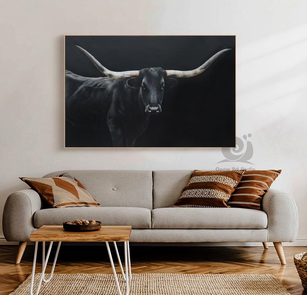 May include: A black and white painting of a longhorn bull with large, curved horns. The bull is centered against a dark background. The artwork is framed and hangs above a gray sofa with decorative pillows.