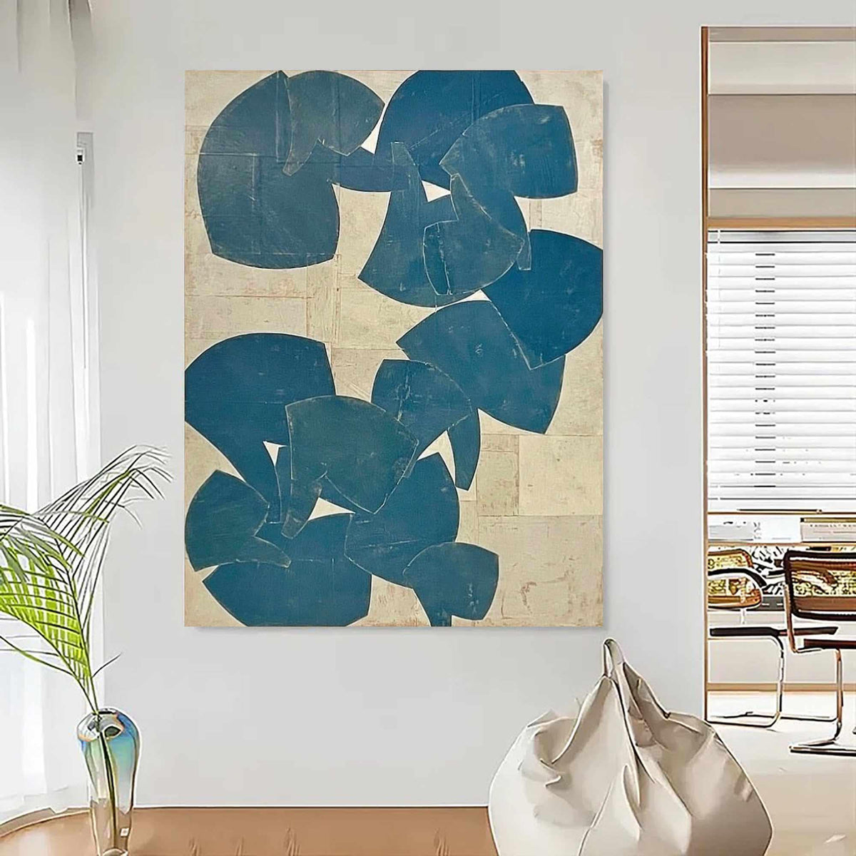 May include: Abstract wall art featuring overlapping blue shapes on a beige background. The artwork has a textured appearance and is displayed in a modern, well-lit room. The shapes vary in size and are arranged to create a dynamic composition.