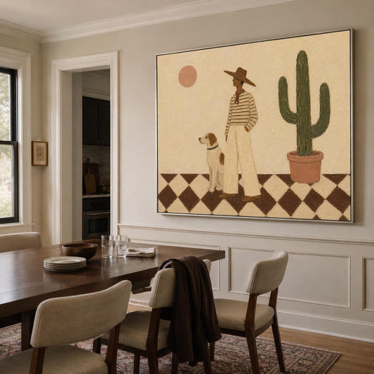 May include: A large rectangular wall art print featuring a person in a wide-brimmed hat and striped shirt standing next to a dog on a checkered floor. A tall green cactus in a terracotta pot and a pale pink sun are visible against a beige background.