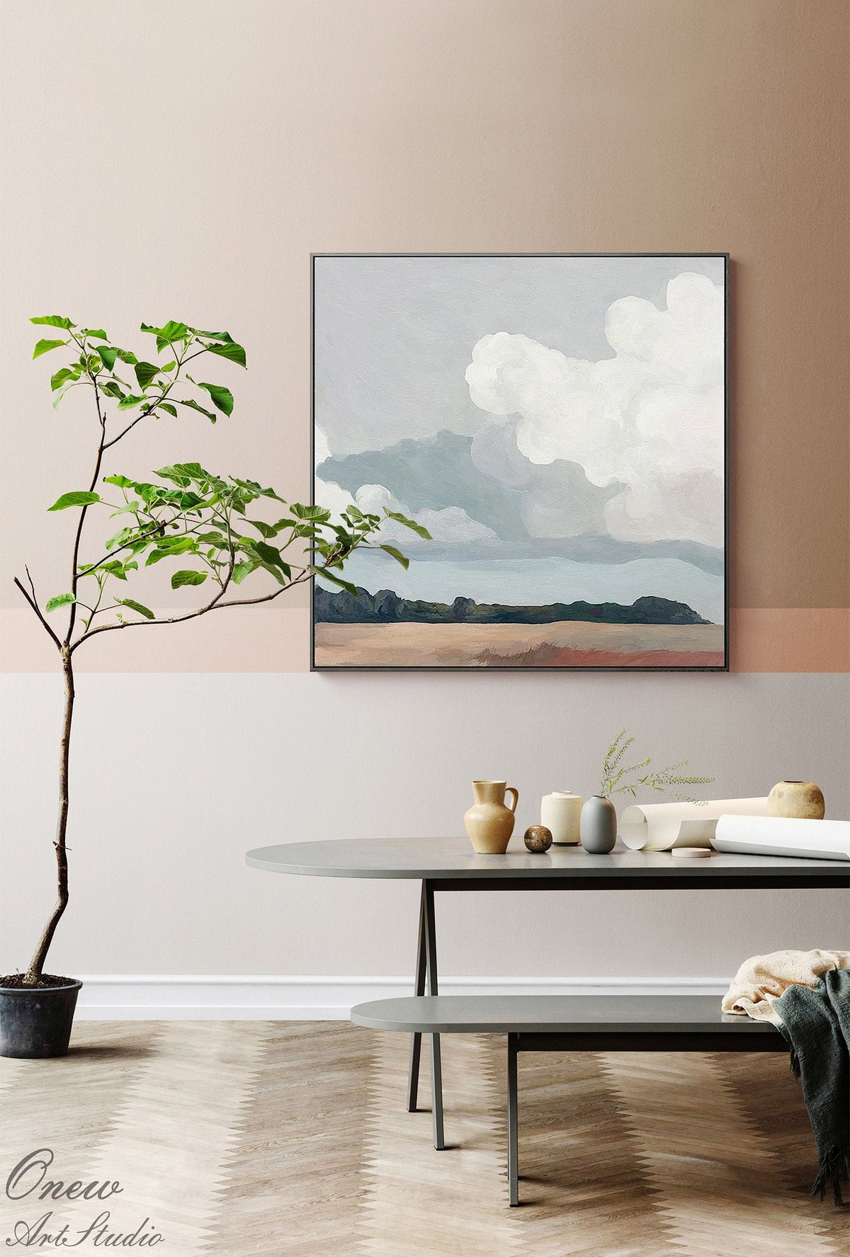 May include: A framed landscape painting depicts a cloudy sky over a distant land. The artwork is displayed in a modern interior with a round table, decorative vases, and a small potted tree. The color palette includes muted blues, browns, and grays.