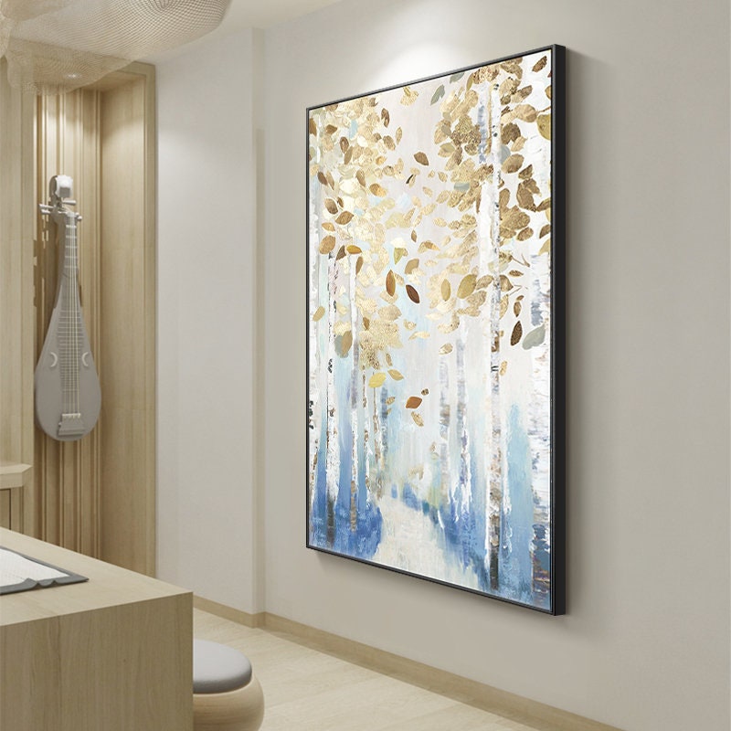 May include: Abstract framed wall art featuring a forest scene with gold and brown leaves, white tree trunks, and blue accents. The artwork is displayed in a room with a light wood desk and a musical instrument.