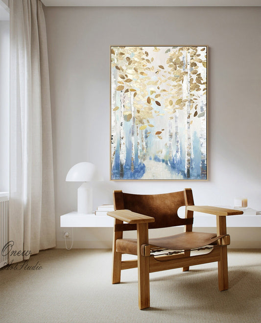 May include: An abstract painting of a birch forest with gold and brown leaves. The artwork features white birch tree trunks with blue and gold accents. The painting is framed in a gold-colored frame and hangs on a light gray wall.