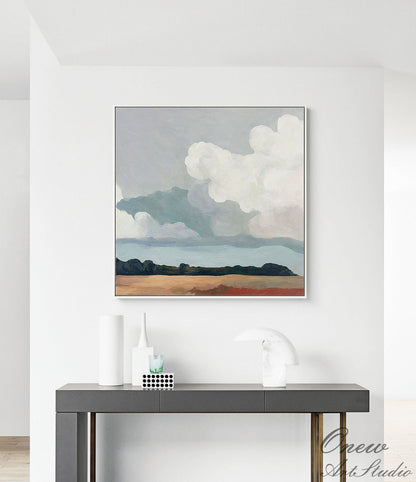 May include: Abstract landscape painting with a silver frame. The artwork depicts a cloudy sky above a field. The color palette includes shades of blue, white, brown, and green. The painting is displayed on a dark gray console table with decorative items.