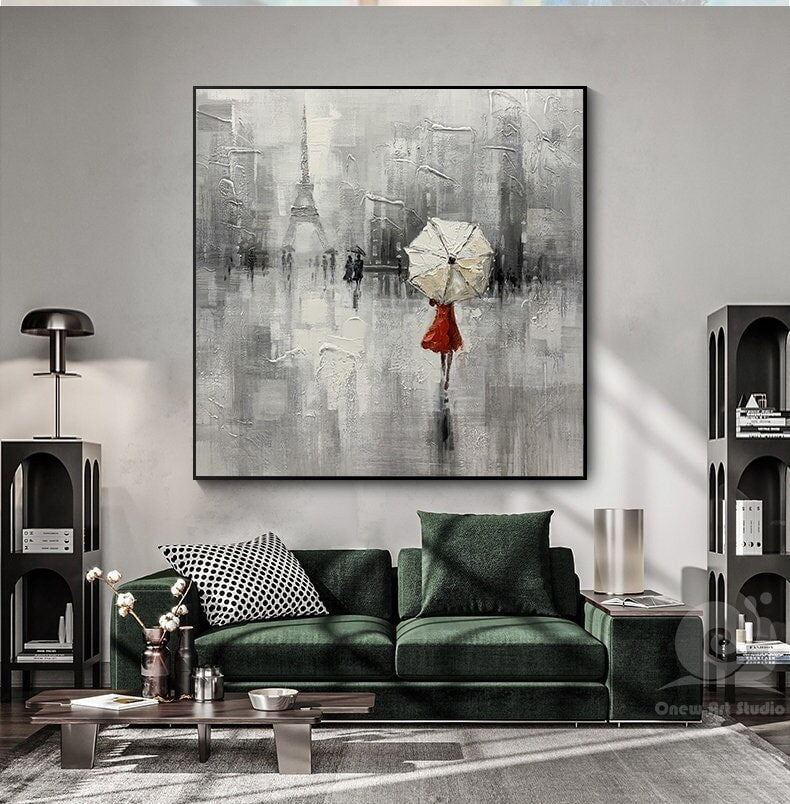 May include: A painting of a woman in a red dress walking in a city with a white umbrella. The background is a gray and white abstract cityscape with a tall building in the distance.