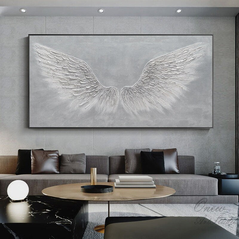 May include: A large abstract painting of white angel wings on a gray background. The wings are textured and appear to be made of feathers. The painting is framed in a black frame.