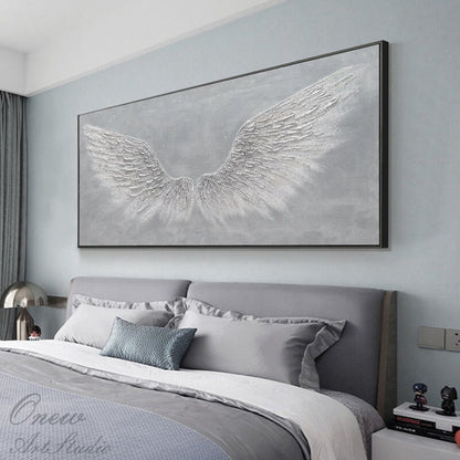 May include: A large, rectangular canvas painting with a gray background and white, textured angel wings. The painting is hanging on a wall above a gray headboard and bed.