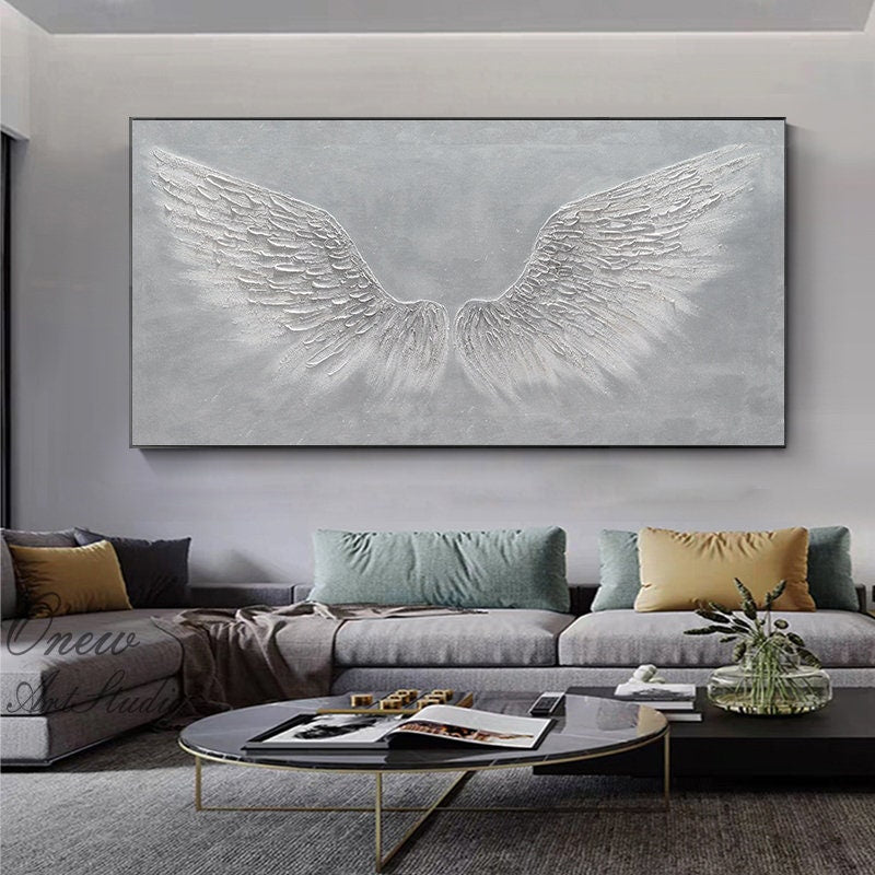 May include: A large abstract painting of white angel wings on a gray background. The wings are textured and appear to be made of feathers. The painting is hanging on a wall in a living room setting.