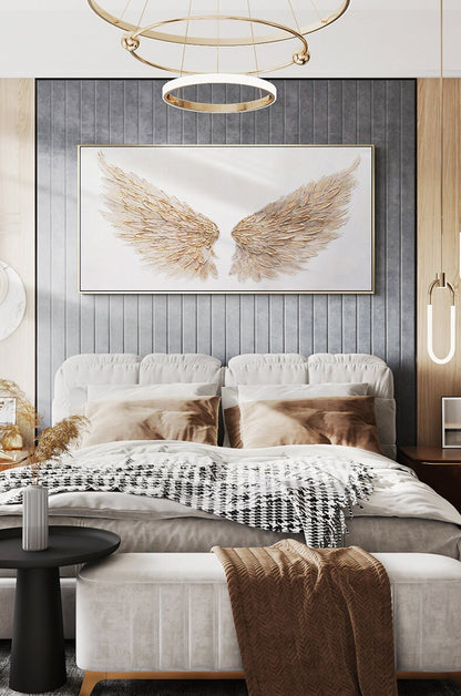 May include: A bedroom scene featuring a large framed artwork of gold-colored angel wings above a bed. The bed has a white headboard, brown pillows, and a black and white patterned blanket. A bench and side table complete the decor.
