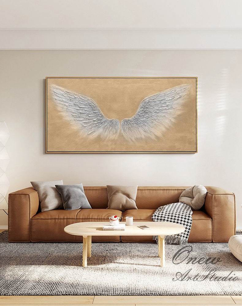 May include: A large abstract painting of white angel wings on a beige background. The painting is framed and hanging on a wall in a living room.
