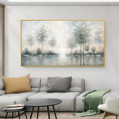 May include: A landscape painting featuring a serene waterscape with trees. The artwork, framed in gold, depicts a misty scene with soft blues, greens, and whites. The painting is displayed above a gray sectional sofa with accent pillows.