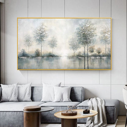 May include: A landscape painting featuring a serene waterscape with trees. The artwork is framed in gold and depicts a misty scene with soft blues, grays, and whites. The painting evokes a sense of calm and tranquility, suitable for home decor.