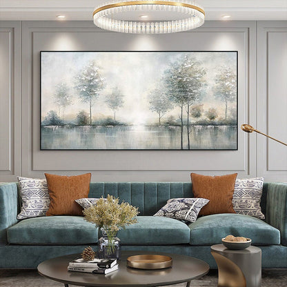 May include: A large rectangular landscape painting with a black frame. The artwork depicts a serene scene of trees reflected in a body of water, with soft, muted colors of gray, white, and blue. The painting hangs above a teal sofa with decorative pillows.
