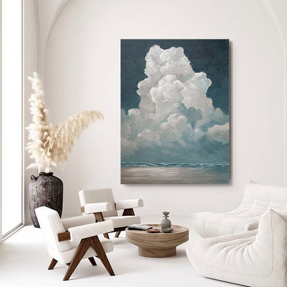May include: A large canvas painting depicts a dramatic cloud formation over a seascape. The artwork features a dark blue sky, fluffy white clouds, and a muted blue and beige horizon. The painting is displayed in a modern, minimalist living room.