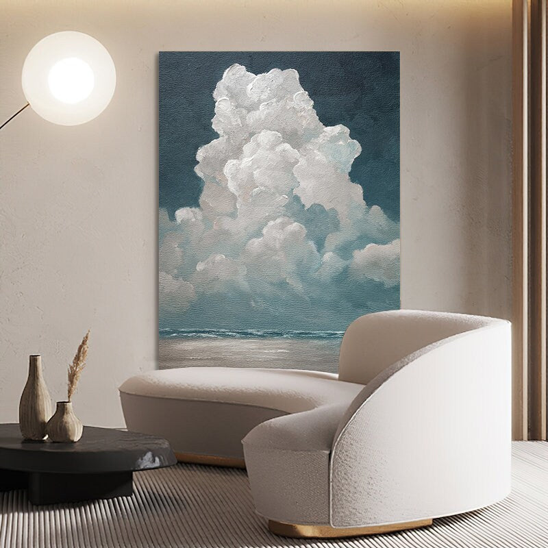 May include: A large canvas art print depicts a dramatic cloud formation over a seascape. The artwork features a palette of blues, whites, and grays, creating a serene yet powerful atmosphere. The painting is displayed in a modern living room setting.
