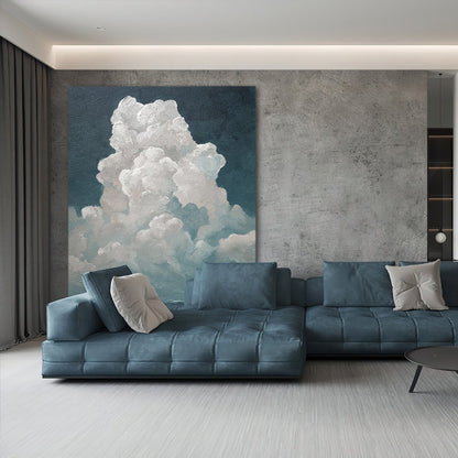 May include: A large canvas painting depicts a cloud formation in shades of white and blue against a dark blue background. A modern blue sectional sofa with square cushions and throw pillows sits below the artwork, creating a cohesive living room design.