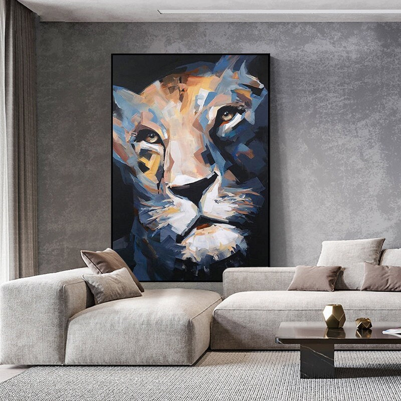 May include: Abstract lion portrait painting with a black frame. The artwork features a close-up of the lion's face, rendered in shades of blue, tan, and white. The painting is displayed in a modern living room setting.