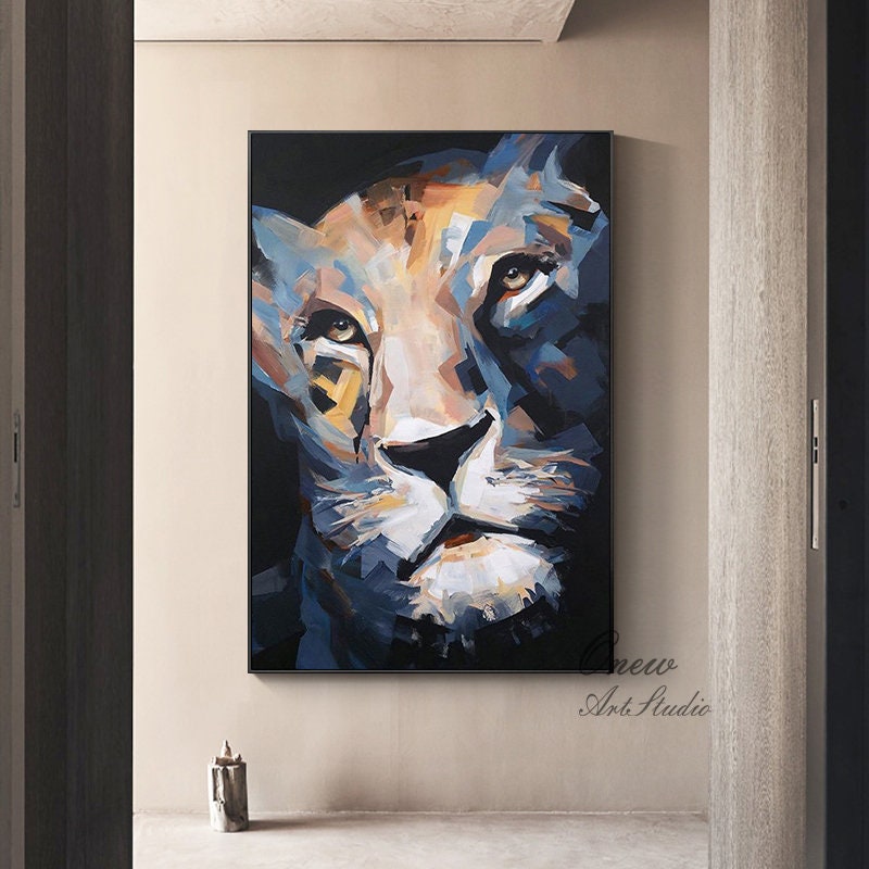 May include: A framed abstract painting of a lion's face. The artwork features a palette of blues, whites, and yellows, with a black background. The lion's eyes are brown. The painting is displayed in a modern interior setting.