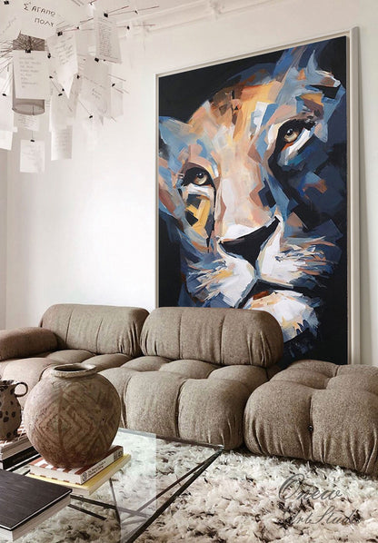 May include: Large framed abstract painting of a lion's face in shades of blue, gold, and white. The artwork is displayed above a brown sectional sofa and a glass coffee table. The room has a modern, minimalist design.