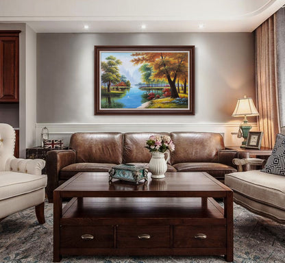 May include: A living room interior with a brown leather sofa, a coffee table, and a framed landscape painting of a lake and trees. The painting is in a brown frame and has a blue and green color scheme.