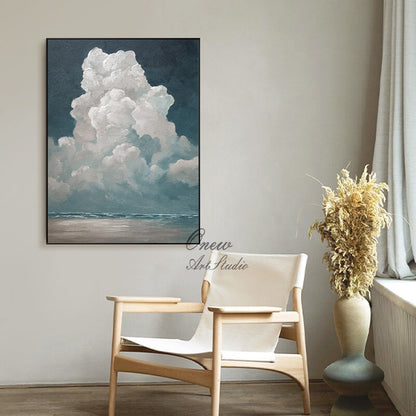 May include: An abstract painting of a large, fluffy white cloud against a dark blue sky. The artwork, framed in black, depicts a seascape at the bottom. The scene is set in a room with a wooden chair and a vase with dried plants.