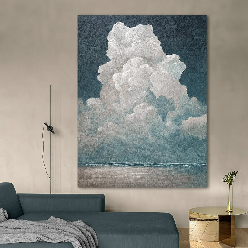 May include: Large canvas art print depicting a dramatic cloud formation over a seascape. The artwork features a dark blue sky, fluffy white clouds, and a calm ocean with a sandy beach. The painting is displayed in a modern living room setting.