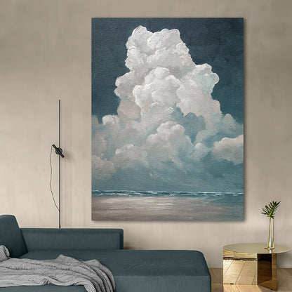 May include: Large canvas art print depicting a dramatic cloud formation over a seascape. The artwork features a dark blue sky, fluffy white clouds, and a calm ocean with a sandy beach. The painting is displayed in a modern living room setting.