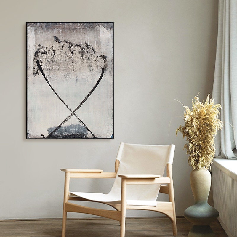 May include: A black and white abstract painting with a light gray background. The painting features two thick black lines that cross in the center of the canvas. The lines are slightly curved and create a sense of movement. The painting is framed in a black frame and is hanging on a white wall.