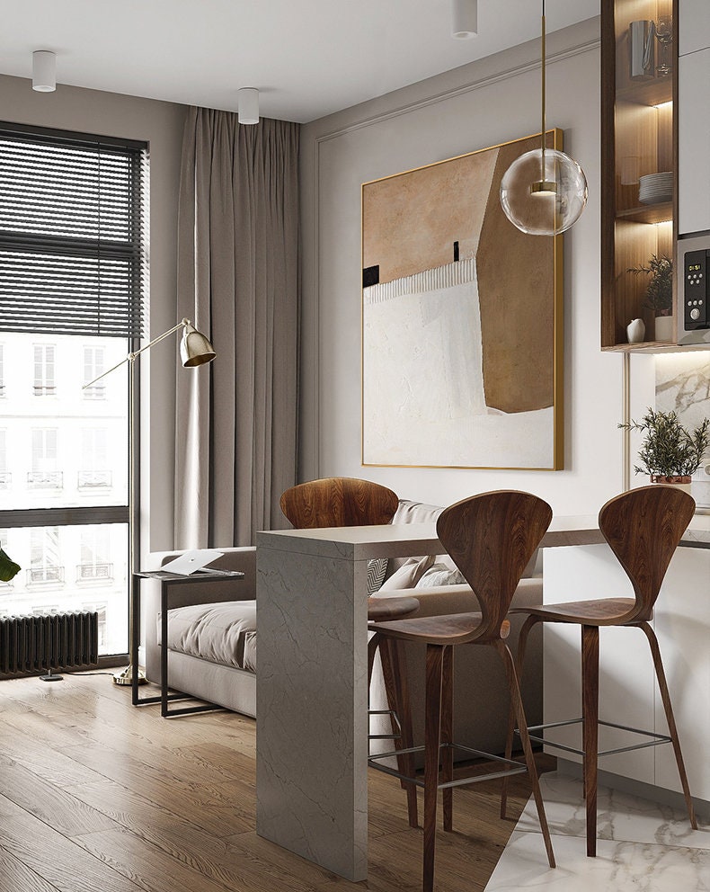 May include: A modern kitchen or dining area with a white countertop and two wooden bar stools. The countertop is attached to a wall with a large abstract painting above it. The painting is in shades of brown, white, and black. A glass globe pendant light hangs above the countertop.