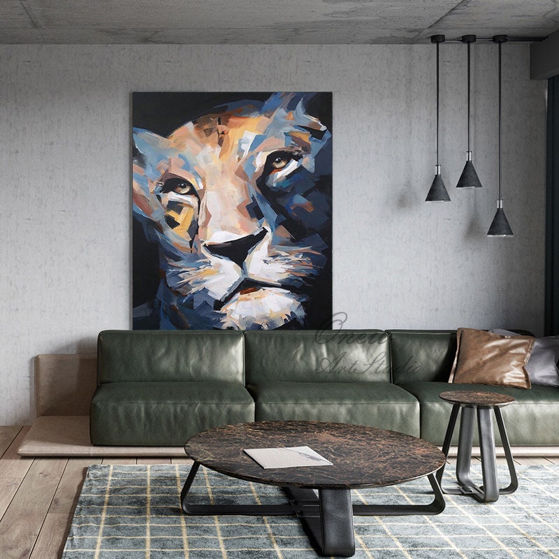 May include: An abstract painting of a lion's face in shades of blue, tan, and white hangs on a gray wall. The artwork is above a green leather sofa and a round coffee table. The room has a modern, minimalist design.