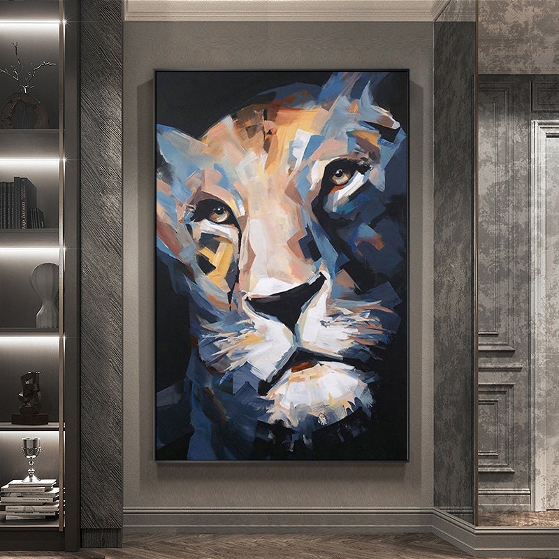 May include: Large framed canvas art featuring a close-up of a lion's face. The artwork uses a palette of blues, oranges, and whites, with visible brushstrokes. The lion's eyes are a focal point, rendered in shades of brown. The painting is displayed in a modern interior setting.