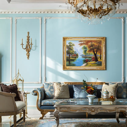 May include: A blue velvet sofa with gold trim and patterned pillows sits in a room with light blue walls and white molding. A framed landscape painting hangs above the sofa. A gold metal table with a glass top sits in front of the sofa.