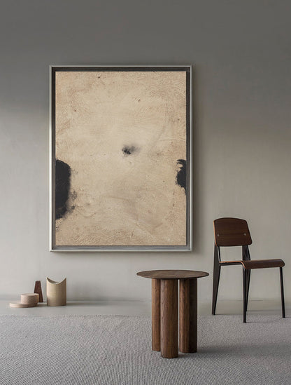 May include: A brown wooden table with a round top and four legs. The table is in a room with a framed abstract painting on the wall and a wooden chair with a black metal frame.