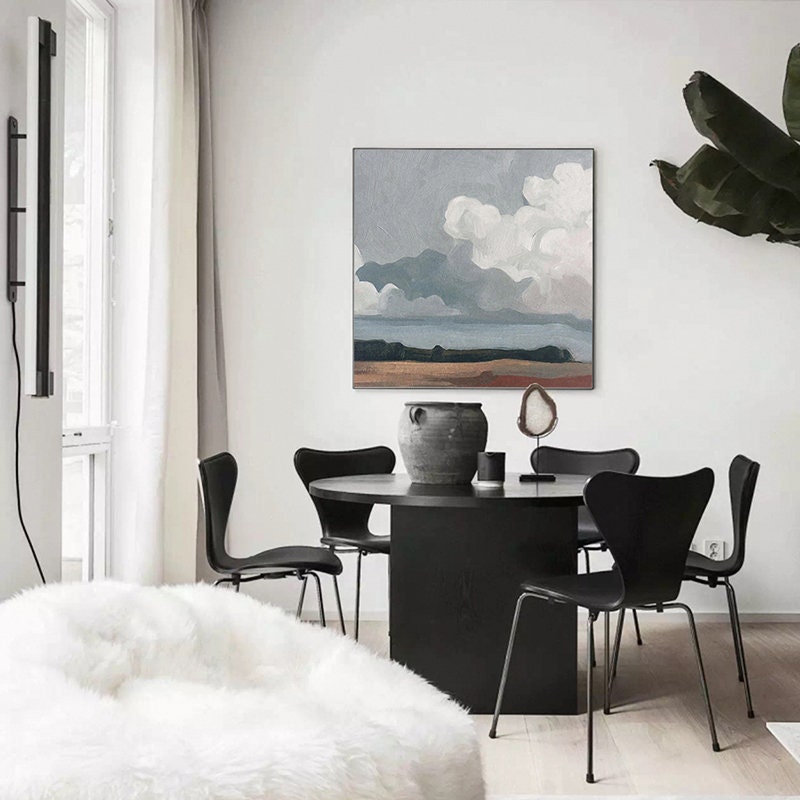 May include: A modern dining room featuring a round black table and four black chairs. A landscape painting with a cloudy sky hangs on the wall. A large, decorative vase and a white, fluffy beanbag chair are also visible.