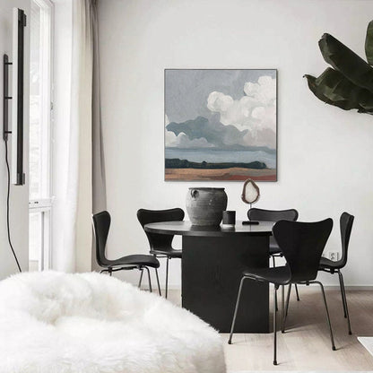 May include: A modern dining room featuring a round black table and four black chairs. A landscape painting with a cloudy sky hangs on the wall. A large, decorative vase and a white, fluffy beanbag chair are also visible.