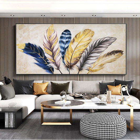 May include: A large abstract painting of gold, blue, and white feathers on a cream background. The painting is framed in a black frame and is hanging on a wall with wood paneling.