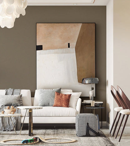 May include: A white sofa with gray and rust colored throw pillows sits in a living room with a brown wall and a large abstract painting above it. A black and white checkered ottoman sits in front of the sofa.