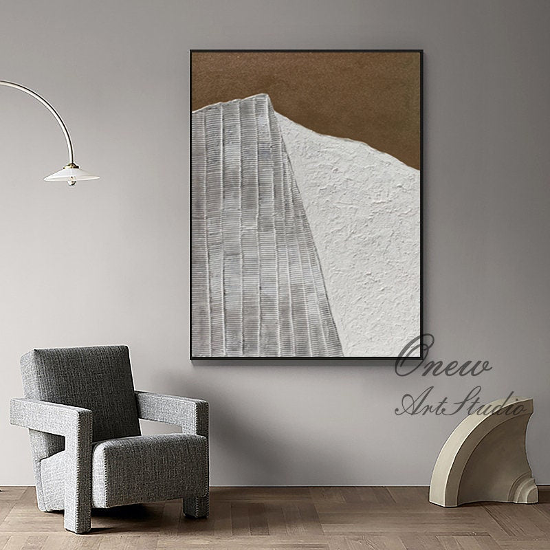 May include: Abstract painting with a white and brown color scheme. The painting features a textured white surface with a geometric pattern in the center. The painting is framed in a black frame.