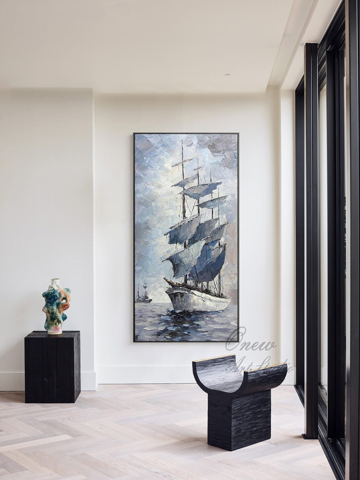 May include: A framed painting of a sailboat with white sails against a blue and gray sky. The sailboat is in the water with a few other boats in the distance. The painting is hanging on a white wall in a modern home.