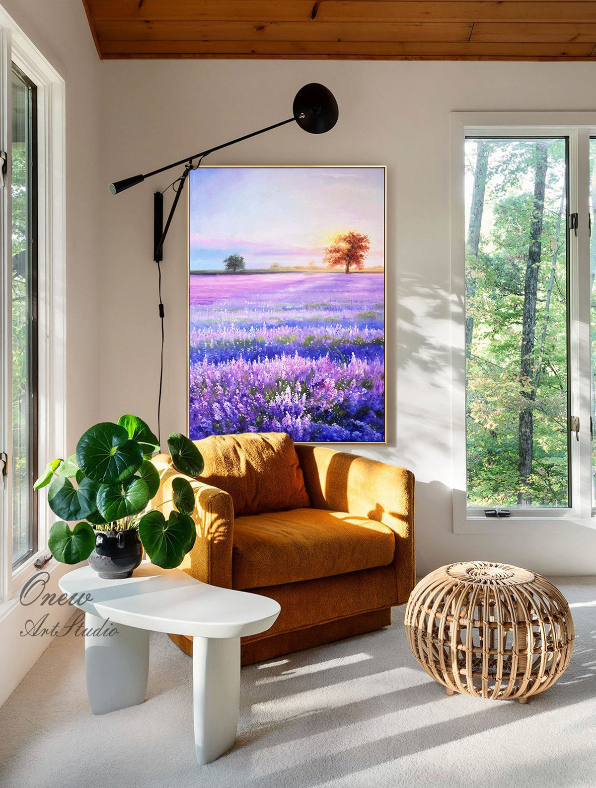 May include: A painting of a lavender field with a single tree in the distance. The painting is hanging on a wall in a living room with a brown armchair, a white side table, and a woven ottoman.
